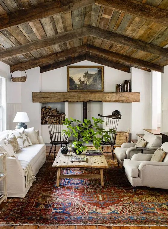 an inviting barn living room with a metal hearth and a wooden mantel, a reclaimed wood ceiling, neutral seating furniture, a printed rug and greenery