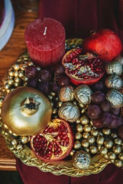 a beautiful and refined fall centerpiece of gilded berries and nuts, grapes, gilded pomegranates and a bold red candle