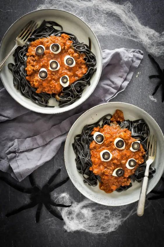 black pasta with tomato and cheese on top and egg and olive eyeballs for Halloween parties
