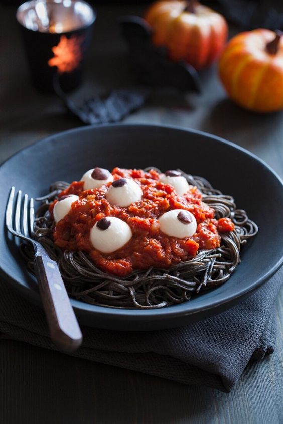 black pasta with tomato sauce and eyeballs is a spooky and bold Halloween food idea to make yourself
