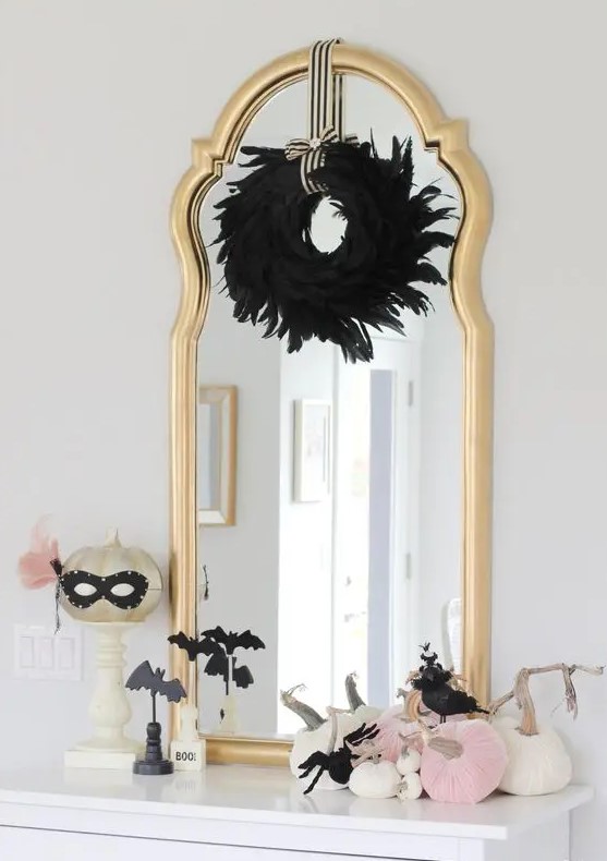 glam Halloween styling with a black feather wreath, a gold pumpkin in a mask, pink and white pumpkins and black bats