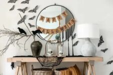 13 a cool Halloween console table styled with black cheesecloth, baskets and blankets, a vase with branches, bats and blackbirds, a couple of banners