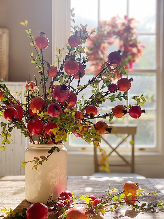 a fall centerpiece of a jar with greenery and branches with pomegranates is a catchy idea that is easy to repeat