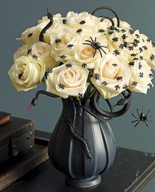 a beautiful and scary Halloween centerpiece of a black vase with white roses and spiders plus a black snake