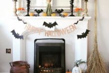 17 a Halloween mantel with bats, candles, pumpkins, orange blooms, a wheat bundle and some pumpkins and a broom on the floor