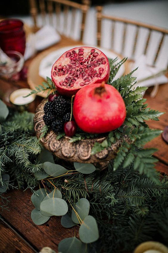 a gorgeous fall to Christmas centerpiece of blackberries, cherries, pomegranates and greenery in a vintage urn