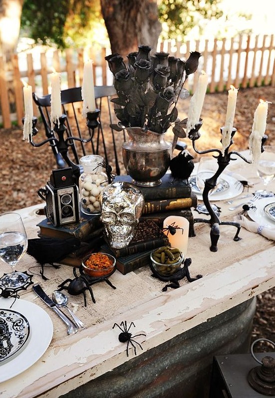 a bold Halloween tablescape with black and white porcelain, black candelabras, books, skulls, black flowers and black spiders for a scarier feel