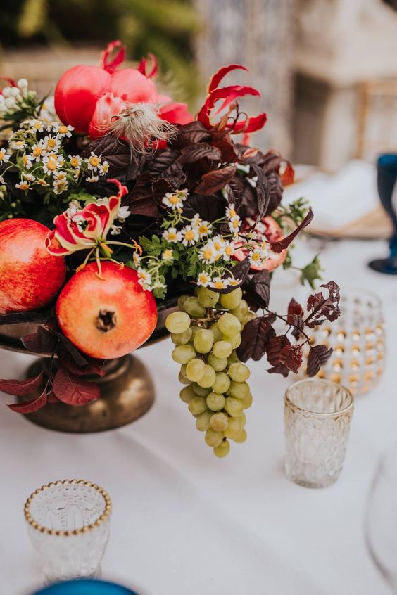 a lush centerpiece of chamomiles, dark foliage, pomegranates, bold blooms and grapes is great for your tablescape