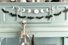 21 a black bat garland paired with a white moon phase one are a cool and simple combo for Halloween decor