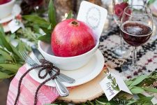 21 a lush fall or Thanksgiving tablescape with a checked runner, greenery, wood slices placemats, a striped napkin, a bowl with a pomegranate