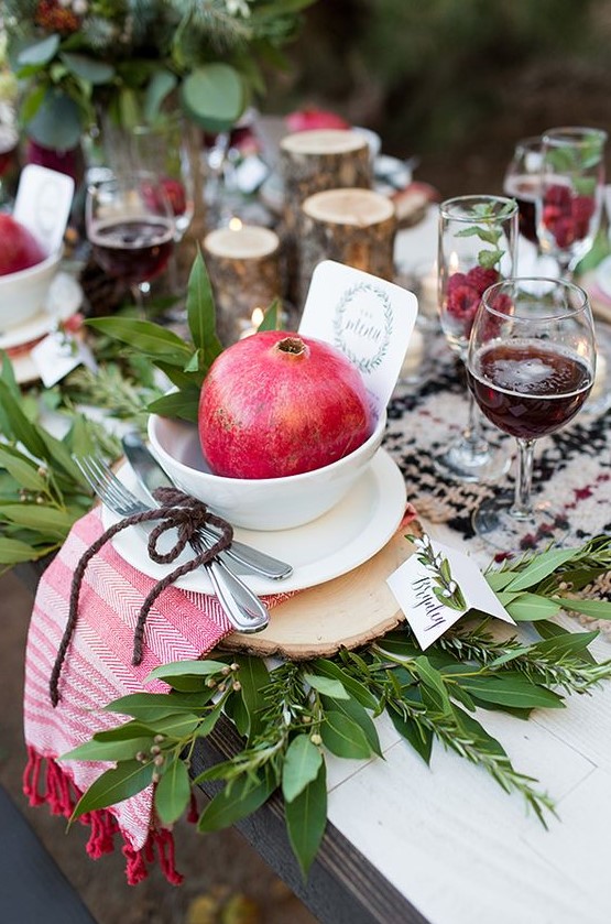 a lush fall or Thanksgiving tablescape with a checked runner, greenery, wood slices placemats, a striped napkin, a bowl with a pomegranate