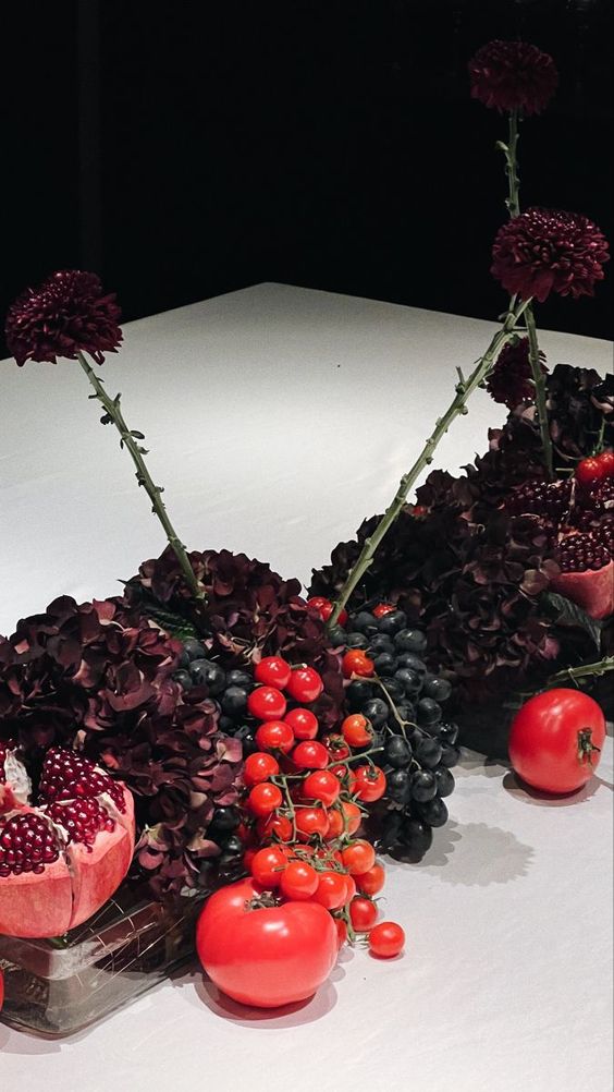 a moody centerpiece of tomatoes, a pomegranate, dark hydrangeas, grapes and dark dahlias is amazing for fall or Thanksgiving