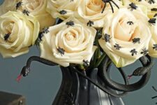23 a Halloween centerpiece of a black vase with white roses, black snakes, spoders and flies is a catchy and bold idea