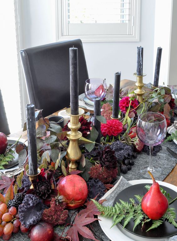 a moody Thanksgiving tablescape with dark fruit and blooms, dark foliage, black candles in gold candleholders, black and white plates and pears