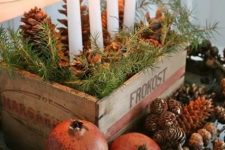24 a rustic centerpiece of a crate with evergreens and pinecones plus candles and pinecones and pomegranates around