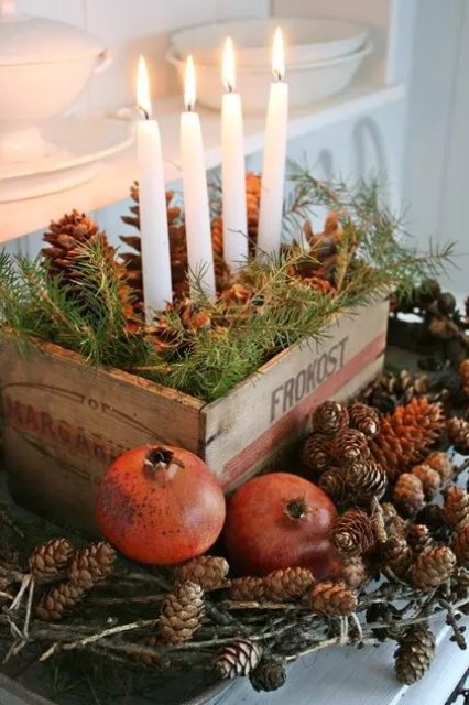a rustic centerpiece of a crate with evergreens and pinecones plus candles and pinecones and pomegranates around