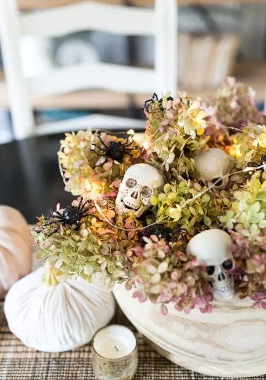 a neutral bowl with dried hydrangeas, skulls, spiders, lights and white velvet pumpkins for Halloween