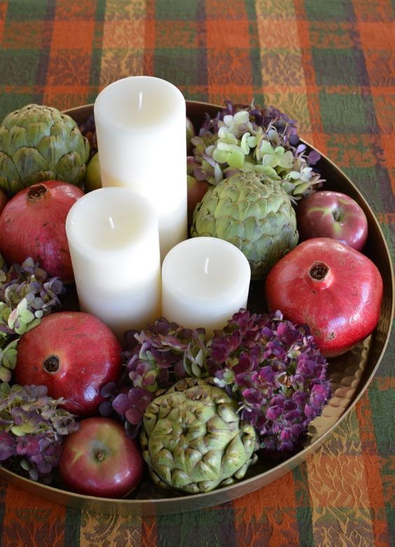 a rustic centerpiece of green and purple hydrangeas, apples, pomegranates, artichokes and pillar candles