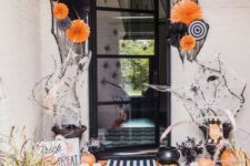 26 a bold and whimsical Halloween porch with paper fans, buntings, orange and white pumpkins, spiders and branches