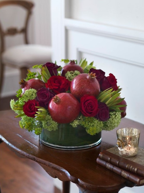 a rustic fall centerpiece of green blooms, red roses, pomegranates is a cool and pretty arrangement