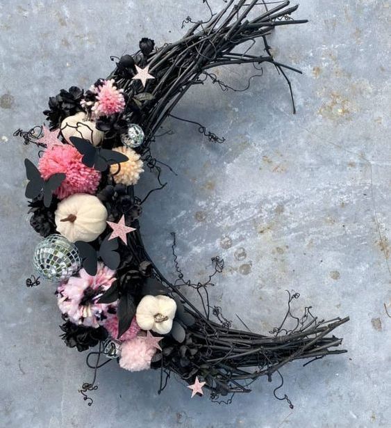 A creative moon shaped Halloween wreath with pink pompoms, little pumpkins, black butterflies, a disco ball and some stars