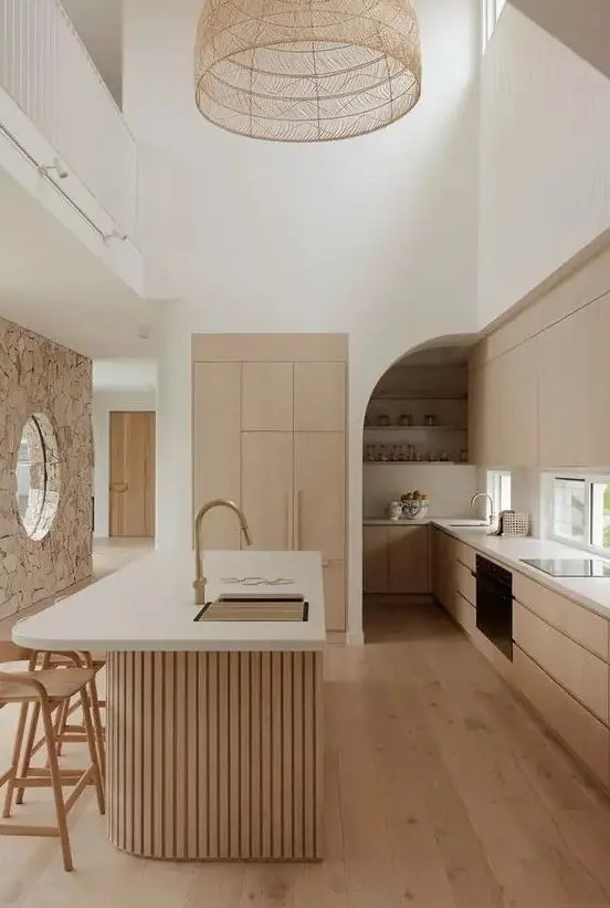 A light stained minimalist kitchen with sleek cabinets, a window backsplash, a curved fluted kitchen island with a curved part and a woven pendant lamp