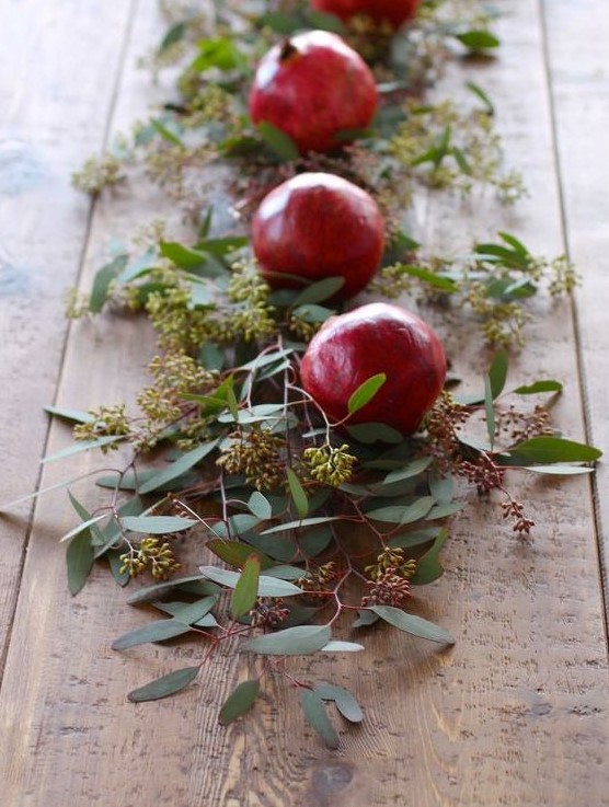 a table runner of seeded eucalyptus and pomegranates is a cool idea to style your table for fall or winter