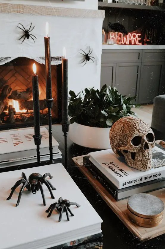 stylish Halloween decor with black candles in candleholders, black spiders, a beautiful ornated skull abd some spiders on the fireplace