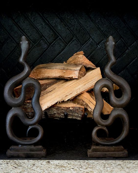 A non working fireplace with firewood accented with two black snake stands is a creative and scary idea