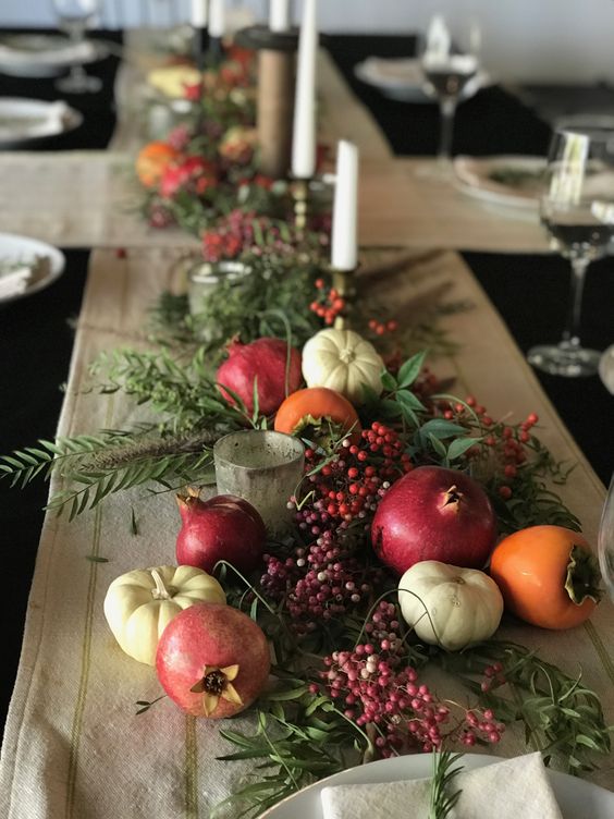 bold and catchy fall table decor with pomegranates, pumpkins, some fruit, greenery and candles is lovely