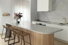 37 a minimalist white kitchen with fluted cabinets, a white marble backsplash, a curved kitchen island with a stone countertop