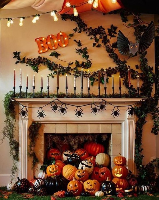 A jaw dropping Halloween mantel with a moss garland and lots of candles, greenery on the wall, lots of colorful pumpkins and jack o lanterns in the fireplace