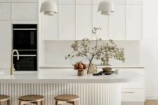 41 a sophisticated contemporary kitchen in white, with a white stone backsplash and countertops, a curved fluted kitchen island, pendant lamps