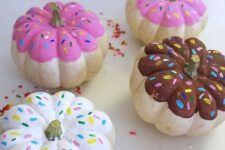60 colorful pumpkins painted as glazed donuts with sprinkles for a fun and quirky touch