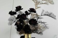 a Halloween arrangement of very dark, almost black roses and some branches in black and gold vases