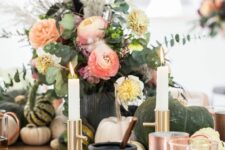 a Halloween centerpiece of coral and white and yellow blooms, greenery, twigs and feathers is a cool arrangement