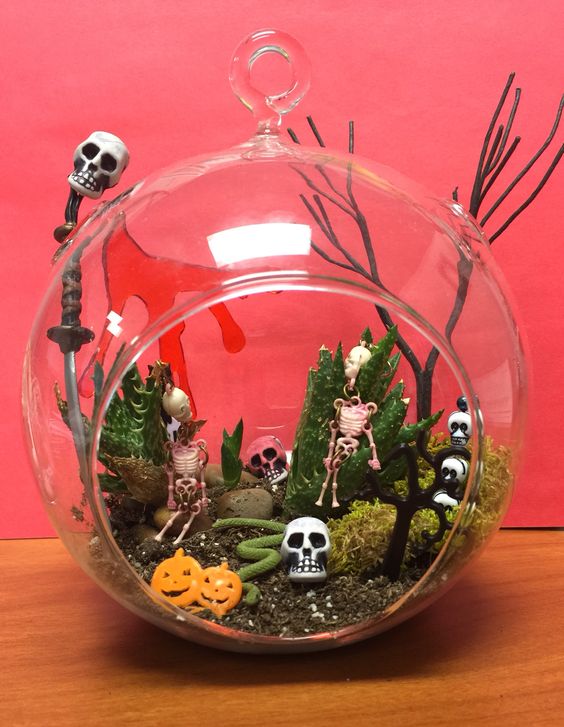 A Halloween terrarium with moss, faux succulents, skulls, skeletons, jack o lanterns and a snake is easy to make