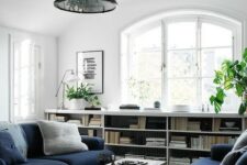 a Scandinavian living room with bookshelves, navy sofas, a coffee table, potted plants and a black pendant lamp