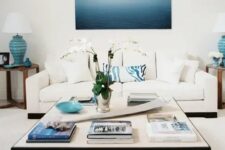a beahcy living room in cremay and bold blues, a modern coffee table, a large and bold artwork, side tables with blue lamps