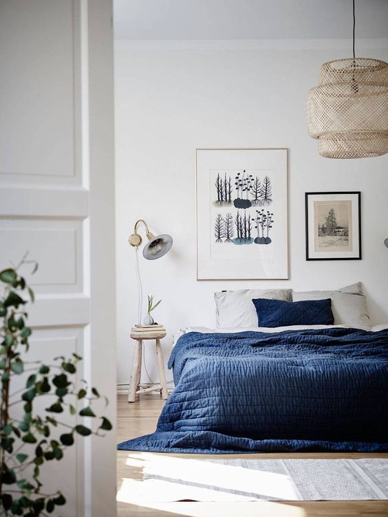 a beautiful and airy bedroom with a bed with grey and navy bedding, a rug, a gallery wall and a nightstand