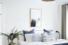 a beautiful and contrasting coastal bedroom with a white bed, navy and white bedding, a wooden stool and eucalyptus and a woven pendant lamp