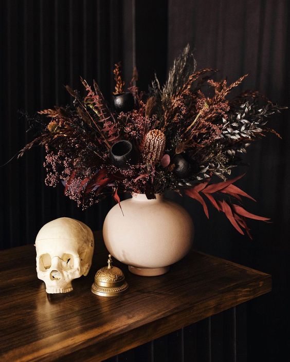 A beautiful and moody Halloween wedding centerpiece of dark and burgundy grasses, foliage and some seed pods looks jaw dropping