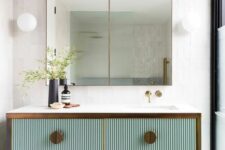 a beautiful bathroom nook with a mint green fluted vanity with brass knobs and framing, a double mirror and some greenery