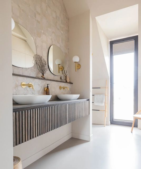 a beautiful neutral bathroom wiht a reeded built-in vanity, vessel sinks, irregular-shaped mirrors, gold fixtures is wow