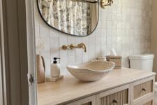 a beautiful neutral bathroom with Zellige tiles, a large reeded vanity, a bowl sink, an irregular-shaped mirror and some chic decor