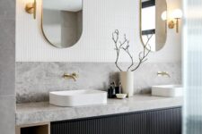 a beautiful stone vanity with a reeded door and open storage compartments, vessel sinks, gold fixtures and oval mirrors