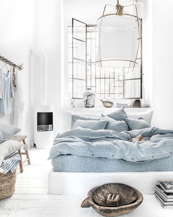 a boho coastal bedroom done in white, with blue bedding, a paper lamp, wooden furniture, baskets and some blue textiles