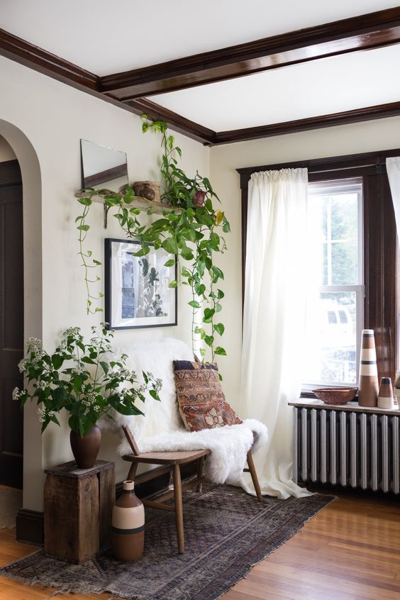 A boho space with dark stained wooden beams, a wooden bench and a stool, vases and potted greenery