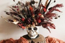 a bold Halloween arrangement in a skull, with dried grasses and blooms plus leaves is a catchy Halloween decoration