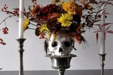 a bold Halloween centerpiece of a bowl holding a skull with super bright blooms, candlesticks and tall and thin candleholders